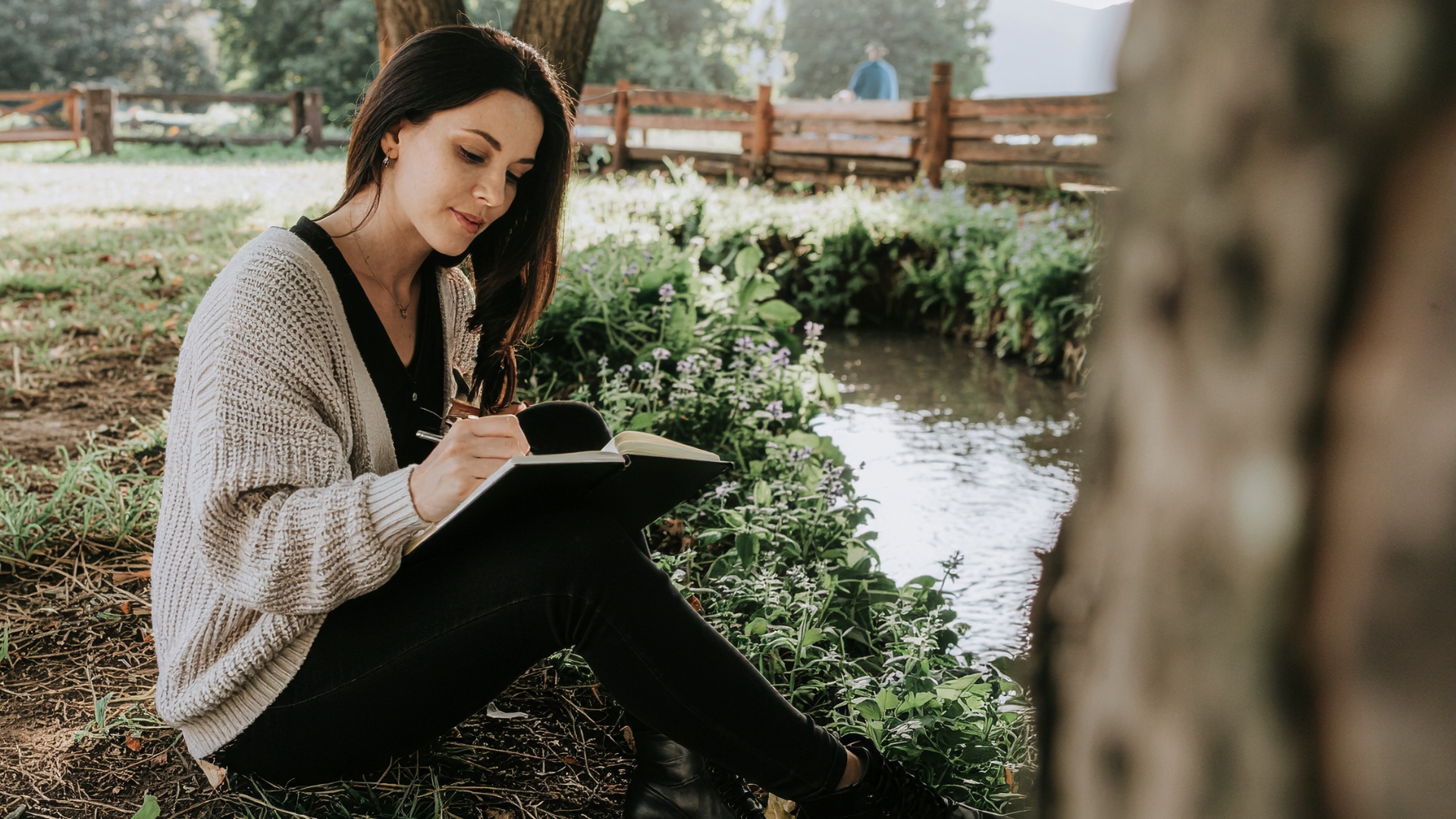 Woman journaling outdoors by a stream — a moment of reflection